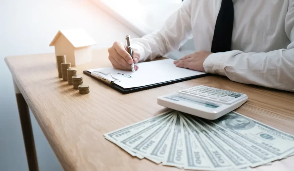 A landlord signing a rental property agreement at a desk with stacked coins, dollar bills, and a calculator symbolizing the financial risks of self-managing.